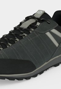 Gros plan d'une basket gris foncé et noire avec des lacets rayés noirs et gris et deux bandes latérales gris clair.