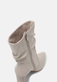 Stivale alla caviglia beige realizzato in pelle liscia, con punta a punta, design morbido e cerniera laterale con accessori in argento.