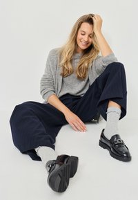 Gray sweater, navy pinstriped wide-leg trousers, gray socks with scalloped edges, and black loafers with a chain detail and textured sole.