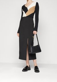 Maglietta nera a maniche lunghe con audaci motivi geometrici in crema e beige, abbinata a una gonna maxi nera aderente con spacco frontale e mocassini neri.