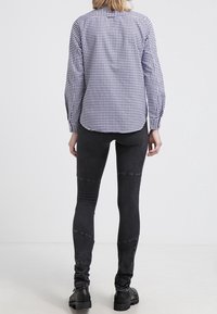 Camicia button-down con motivo a quadri navy e bianchi, abbinata a leggings neri con dettagli a cucitura e una texture liscia.