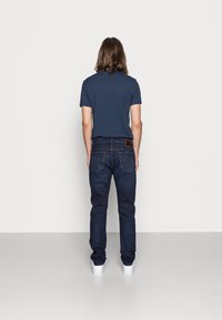 Marineblå kortermet T-skjorte i kombinasjon med m�ørk denimjeans. Hvite joggesko kompletterer det uformelle antrekket. Enkelt design og rene linjer er tydelige.