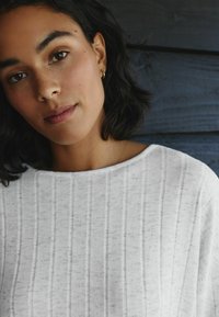 Weißer Rippstrickpullover mit weitem Ausschnitt und weicher Textur. Der Stoff weist subtile Variationen auf, die das visuelle Interesse steigern.