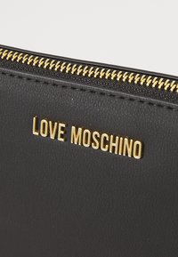 Μαύρο δερμάτινο αξεσουάρ με χρυσό φερμουάρ και χρυσά γράμματα "LOVE MOSCHINO" σε υφή επιφάνειας.