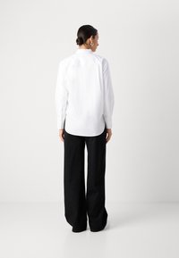 Camicia bianca con maniche lunghe e orlo curvo, abbinata a pantaloni neri a gamba larga con motivi a pois sottili.