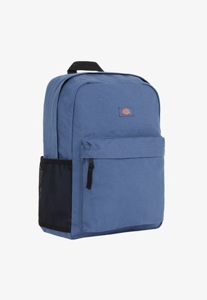 Zaino in tessuto blu con tasca frontale con cerniera, tasca laterale in rete, manico superiore e patch con logo. Forma rettangolare con struttura imbottita.