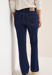 Jeans in denim blu scuro con vita aderente, design a gamba svasata e cuciture visibili. Presentano un'etichetta del marchio sulla vita posteriore e due tasche sul retro.