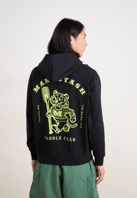 Black hoodie featuring a large green graphic of a tiger holding a paddle, text reading "MANSTASH PADDLE CLUB" and location details.