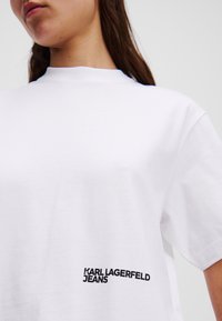 Balta per didelė medvilninė marškinėliai, turintys apvalų kaklą ir trumpas rankoves. Juodas "KARL LAGERFELD JEANS" logotipas šone.