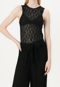 Top de tirantes de encaje negro con un patrón texturizado, que presenta un diseño ajustado, tirantes anchos y un efecto superpuesto transparente.