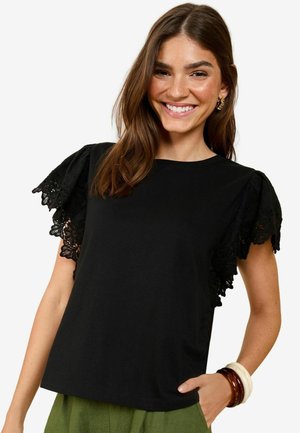 Black short-sleeve t-shirt featuring lace-trimmed puff sleeves. The fabric appears soft and the fit is relaxed. Worn with green pants.