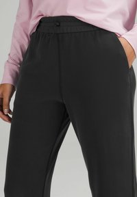Svarta träningsbyxor med resårmidja och dragsnöre. Slät tygtextur, sidofickor och en avslappnad passform.