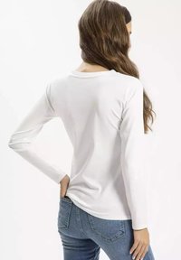 Biała koszulka z długim rękawem, okrągłym dekoltem, gładką fakturą i luźnym krojem, zestawiona z niebieskimi dżinsami. Prosty design.