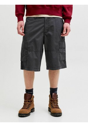 Mand iført mørkegrå cargoshorts, sorte sokker og brune snørestøvler, stående mod en ensfarvet lys baggrund.