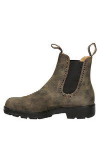 Botín Chelsea de cuero marrón con laterales elásticos, detalles decorativos perforados, lengüetas en la parte trasera y una suela de goma negra robusta.