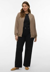 Blouson aviateur beige avec fermeture éclair à l'avant, t-shirt noir, pantalon large noir, et ballerines beige. Textures lisses et lignes épurées.