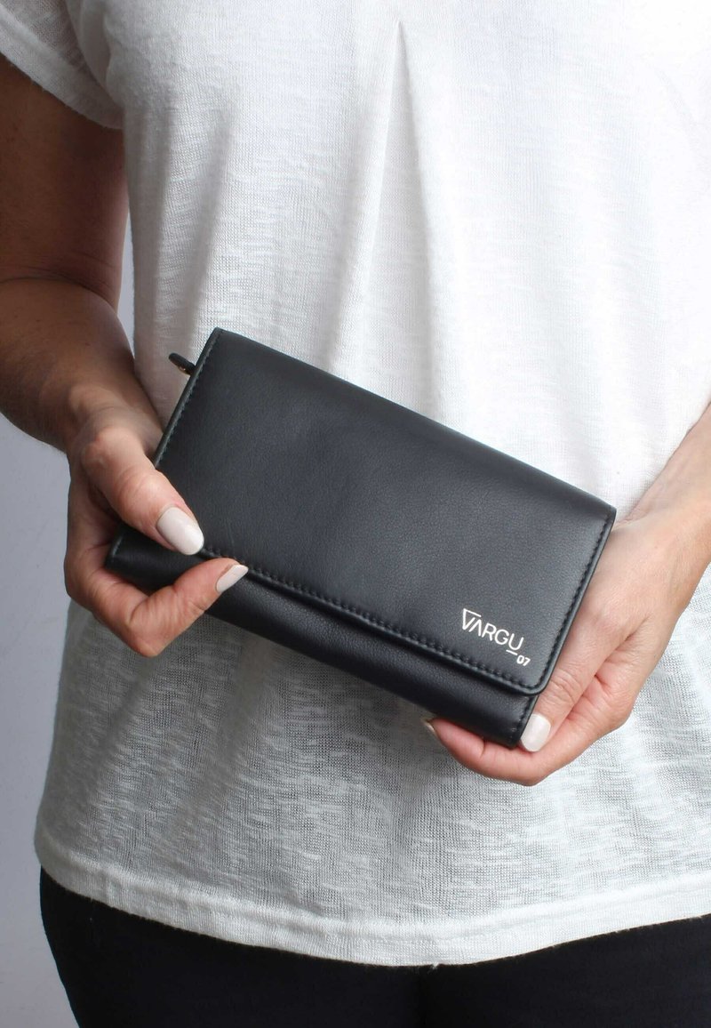 Black leather wallet with a smooth texture, featuring a fold-over design and subtle logo. Held in a person's hand, against a light background.