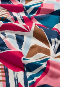 Tissu textile présentant un motif géométrique abstrait en rose, bleu, marron et crème, avec des formes variées et des accents de coups de pinceau.
