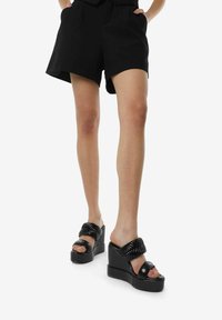 Sandalias de plataforma negras con una suela gruesa y una tira acanalada en la parte superior. Presentan un diseño de punta abierta y una textura de cuero suave.