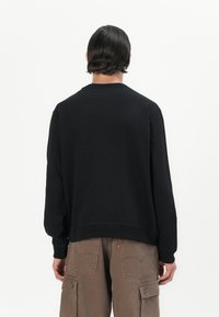 Black sweatshirt with a crew neckline and a relaxed fit, featuring ribbed cuffs and hem. Worn with tan cargo pants.