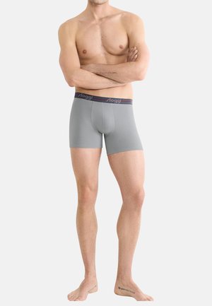 Graue Boxer-Brief von weicher Textur, mit einem dunklen Bund und einem Logo. Das Design ist enganliegend mit einem Schnitt bis zur Mitte des Oberschenkels.