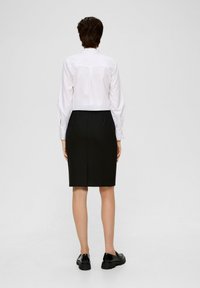 Witte langemouwhemd met een knoopsluiting aan de achterkant, gecombineerd met een zwarte rok tot op de knie en zwarte schoenen. Glad textuur en aansluitend ontwerp.