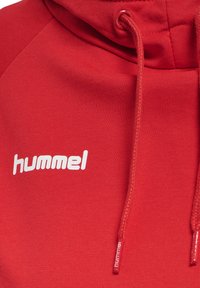 Felpa rossa con cappuccio in tessuto morbido, caratterizzata da una tasca a marsupio, cappuccio con cordino e logo bianco "hummel" sul petto.