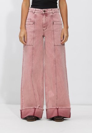 Wijde roze denim broek met grote zijzakken en omgeslagen zomen, gecombineerd met een zwart topje en bruine schoenen.