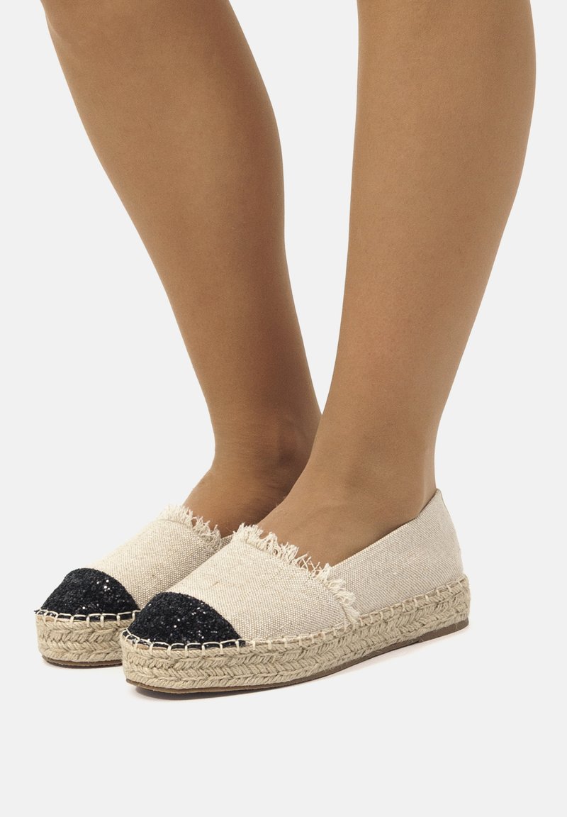 Espadrillas in tela beige con bordi sfilacciati e punta nera glitter, dotate di suola in juta intrecciata. Design casual e leggero.