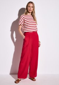 Röd linne-byxor med vida ben, kombinerat med en vit topp med röda ränder. Outfiten har en avslappnad passform och en texturerad look. Bruna sandaler fulländar stilen.
