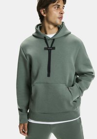 Zöld kapucnis pulóver elülső zsebbel, fekete húzózsinórral és logó díszítéssel. Anyaga sima, textúrált felületű.