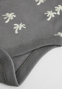 Tessuto di cotone grigio con una superficie liscia, caratterizzato da piccoli motivi di palme bianche. Include un orlo cucito e un collo rotondo confortevole.