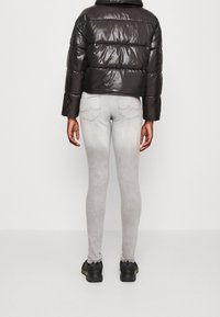 Giacca nera invernale con finitura lucida, design cropped. Leggings grigi con dettagli sottili nella tasca posteriore. Calzature nere completano il look.