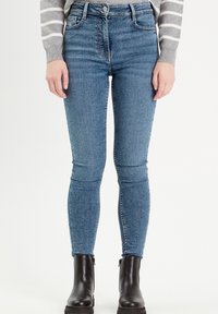 Tight jeans i mellemblå denim med høj talje, der har frontlommer og diskret vaskede detaljer, parret med sorte ankelstøvler.