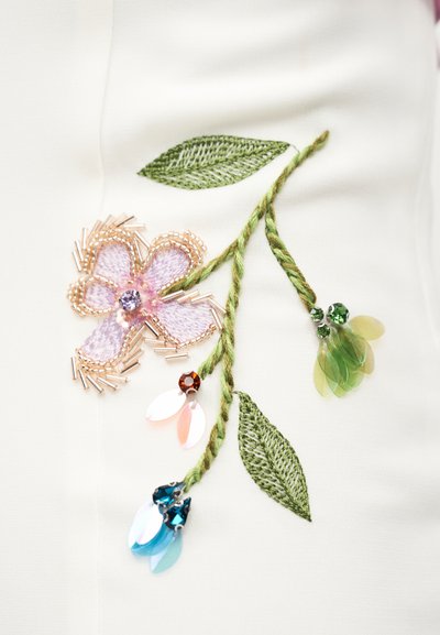 Κεντημένο ύφασμα με πράσινα φύλλα, ροζ λουλούδι περιγραμμένο με χάντρες και τρία στελέχη που καταλήγουν σε μπλε, ροζ και πράσινα λουλούδια με πούλιες.