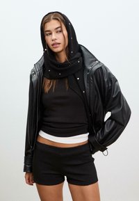 Giacca di pelle nera, top aderente nero, t-shirt bianca, pantaloni corti neri e una sciarpa nera con piccoli dettagli. Tessuto morbido, look stratificato.