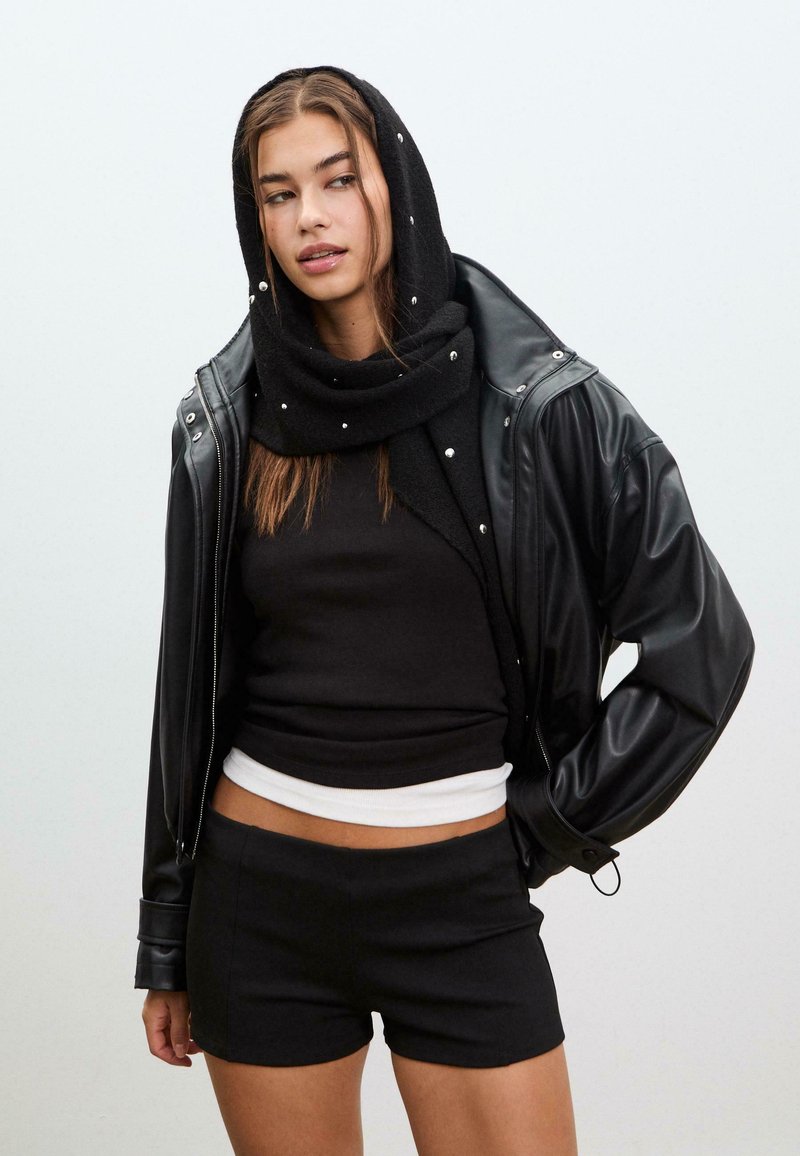 Giacca di pelle nera, top aderente nero, t-shirt bianca, pantaloni corti neri e una sciarpa nera con piccoli dettagli. Tessuto morbido, look stratificato.