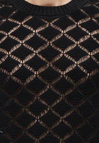 Μαύρο πλεκτό τοπ με μοτίβο διαμαντιού από συμπαγείς και ανοιχτές περιοχές, που αφήνουν να φαίνεται το δέρμα από κάτω, με ριμπ λαιμόκοψη σε στρογγυλό σχήμα.