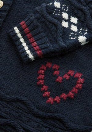 Marineblauer Strickcardigan mit einem roten Herzmuster, ausgestattet mit einem gemusterten Ärmel, der weiße, rote und marineblaue Streifen am Bündchen aufweist.