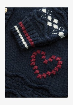 Marineblauer Strickcardigan mit einem roten Herzmuster, ausgestattet mit einem gemusterten Ärmel, der weiße, rote und marineblaue Streifen am Bündchen aufweist.