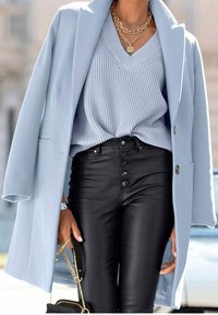 Ljusblå kappa, ribbad ljusblå tröja, högmidjade svarta byxor i konstläder med knapprad, och lager av guldhalsband.