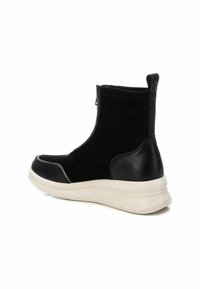 Bottines noires avec un matériau texturé noir et des accents en cuir lisse. Elles disposent d'une fermeture éclair sur le côté et d'une semelle blanche épaisse.