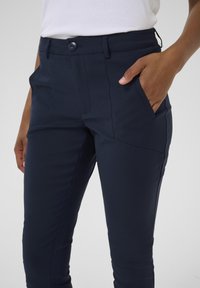 Navy blue tapered pants made from a smooth, stretchy fabric, featuring a front pocket and a fitted design with a button closure.
