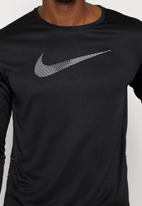 Mann trägt ein schwarzes langärmliges Shirt mit großem weißen Nike-Swoosh-Logo auf der Brust, ab Hals bis zur Taille gezeigt.