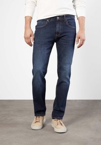 Mörkblå denimjeans med rak passform, med kontrasterande sömmar, fem fickor och en framslutning med knapp, bärs med beige sneakers.