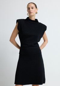 Schwarzes Strickkleid mit einem hohen Kragen, strukturiertem Schulterdesign und figurbetonter Silhouette. Verfügt über einen leichten Glanz und einen seitlichen Schlitz.