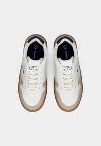 Άσπρα αθλητικά παπούτσια με μπεζ λεπτομέρειες, διάτρητη μύτη, επίπεδη μπεζ σόλα και υφή λευκού άνω μέρους. Διαθέτουν στρογγυλά κορδόνια και εσωτερικό σε ναυτικό μπλε χρώμα.