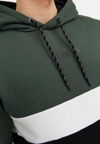 Sudadera con capucha de tela verde con rayas horizontales negras, blancas y azul marino. Cordones negros con detalles rojos y logo visible.