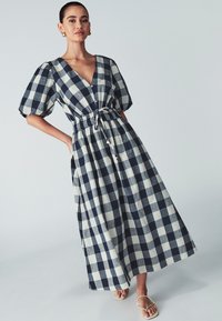 Maxikleid in Marineblau und Creme-Gingham mit Puffärmeln, tiefem V-Ausschnitt, Kordelzug in der Taille und Knopfdetails. Leichte Stoffstruktur.