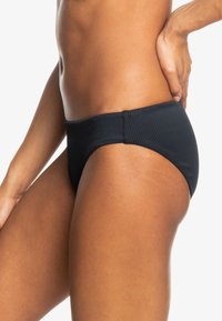 Black ribbed bikini bottom with a smooth waistband, featuring medium coverage and a low-rise cut. Textured fabric adds subtle detail.